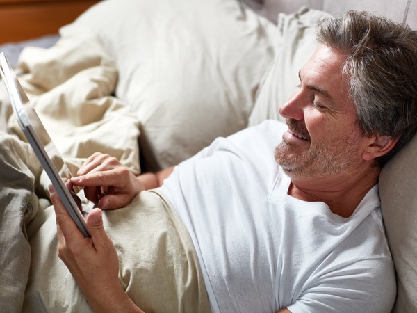 Mann liegt im Bett und liest Schlaftipps auf dem Tablet