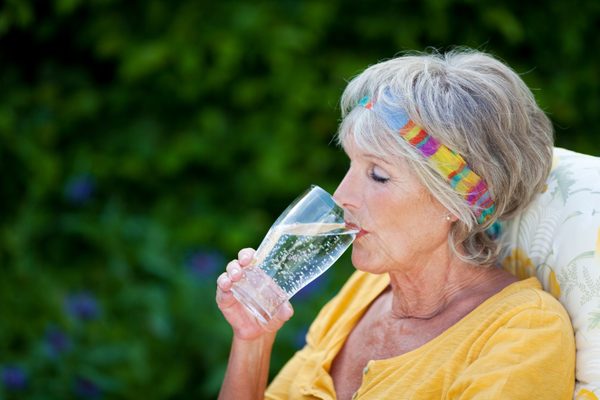 Ältere Frau sitzt auf einem Gartenstuhl und trinkt ein Glas Wasser