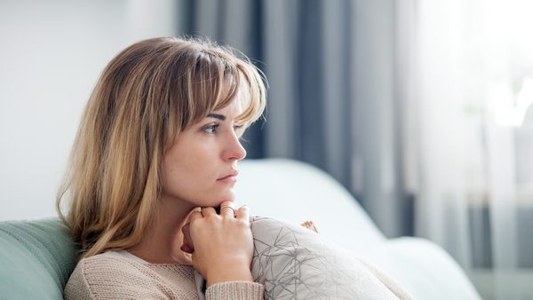 Frau sitzt traurig und nachdenklich auf dem Sofa