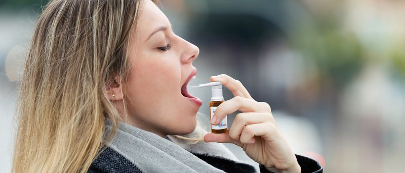 Frau hat Halsschmerzen und sprüht sich ein Arzneimittel in den Mund