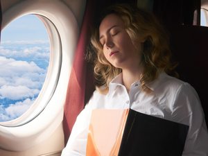 Frau sitzt während einer Flugreise am Fenster und ruht sich bei langem Sitzen aus.
