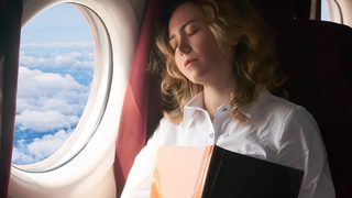 Frau sitzt während einer Flugreise am Fenster und ruht sich bei langem Sitzen aus.