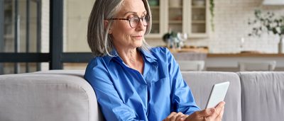 Ältere Frau mit Handy in der Hand auf einer Couch.