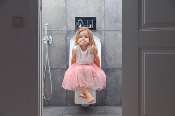 Kleines Mädchen im rosa Kleid sitzt auf Toilette