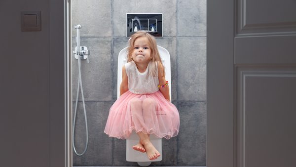 Kleines Mädchen im rosa Kleid sitzt auf Toilette