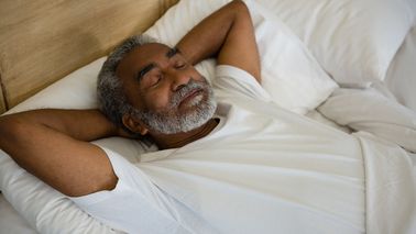 Mann liegt im Bett und schläft erholsam.