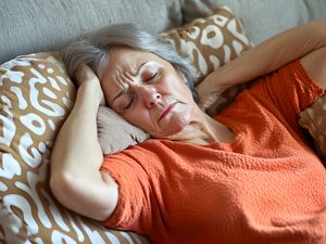 Ältere Frau liegt mit Kopfschmerzen auf dem Sofa und hält den Kopf