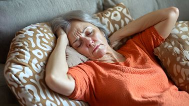 Ältere Frau liegt mit Kopfschmerzen auf dem Sofa und hält den Kopf