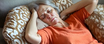 Ältere Frau liegt mit Kopfschmerzen auf dem Sofa und hält den Kopf