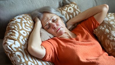Ältere Frau liegt mit Kopfschmerzen auf dem Sofa und hält den Kopf