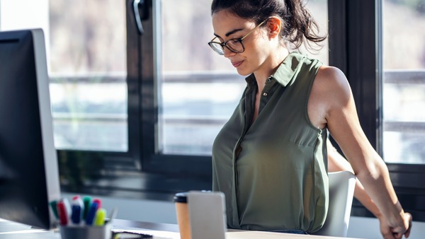Frau sitzt am Schreibtisch und dehnt ihre Arme hinter dem Rücken.
