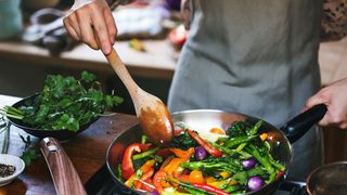 Frau bereitet Gemüse in Pfanne zu.