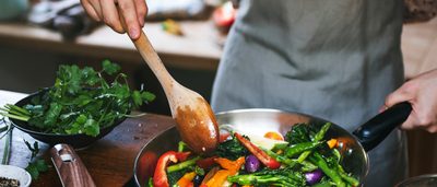 Frau bereitet Gemüse in Pfanne zu.