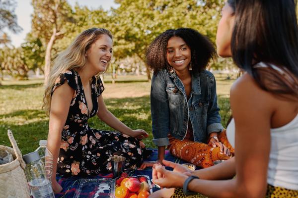 Drei junge Frauen sitzen bei sonnigem Wetter im Park während eines Picknicks.