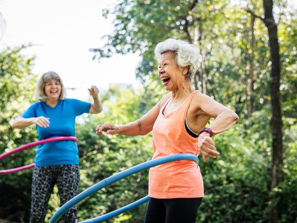 Zwei ältere Frauen machen Hula-Hoop im Grünen.