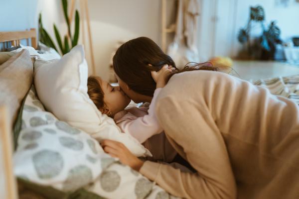Mutter bringt Kind ins Bett und bekommt einen Kuss auf die Wange