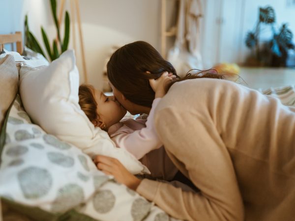 Mutter bringt Kind ins Bett und bekommt einen Kuss auf die Wange