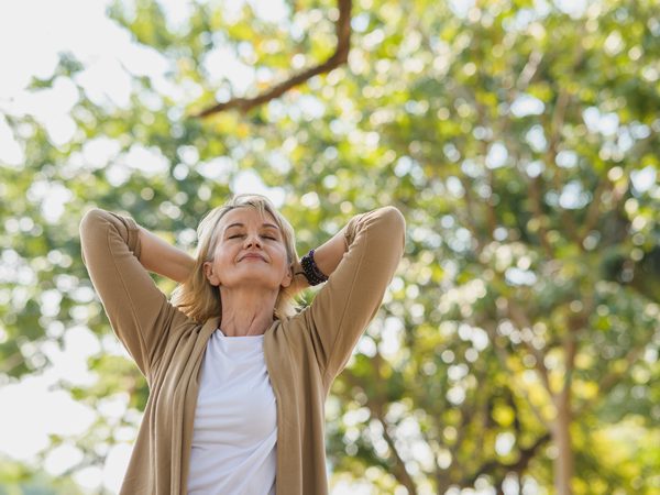 Frau entspannt sich mit geschlossenen Augen im Freien – natürliche Unterstützung bei Kopfschmerzen und Neuralgien.