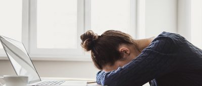 Erschöpfte Frau schläft aufgrund von Schlafmangel mit Kopf auf Schreibtisch