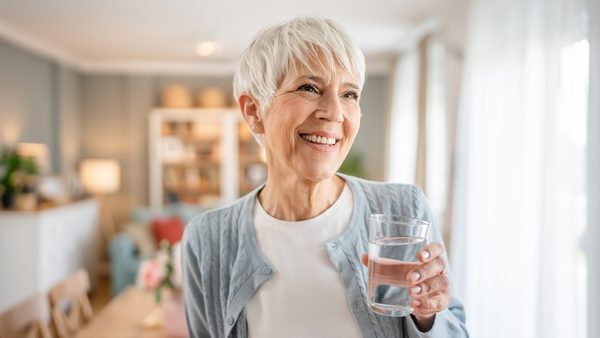Ältere Frau hält ein Glas Wasser in der Hand