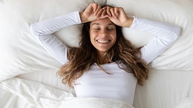 Frau liegt im Bett und lacht.