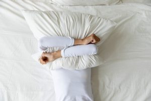 Frau verdeckt ihr Gesicht nach schlafloser Nacht mit einem Kissen