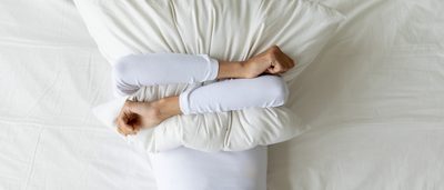 Frau verdeckt ihr Gesicht nach schlafloser Nacht mit einem Kissen