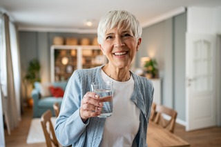 Ältere Frau trinkt ein Glas Wasser gegen Schwindel.