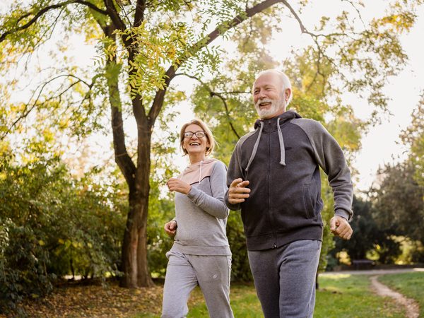Ehepaar geht zügig durch einen grünen Park. Bewegung an der frischen Luft unterstützt die Gelenkgesundheit bei Gicht und rheumatischen Beschwerden.