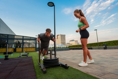 Frau feuert Mann beim Schlittenschieben an.