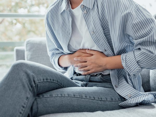 Nahaufnahme einer Person mit Oberbauchschmerz; Hände liegen schützend auf dem Bauch.