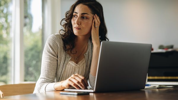 Frau sitzt am Laptop und denkt konzentriert nach