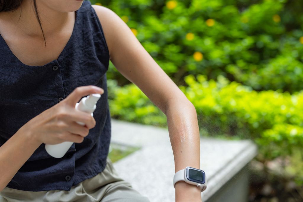 Frau sprüht ein Mückenspray auf den Arm