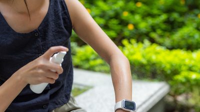 Frau sprüht ein Mückenspray auf den Arm