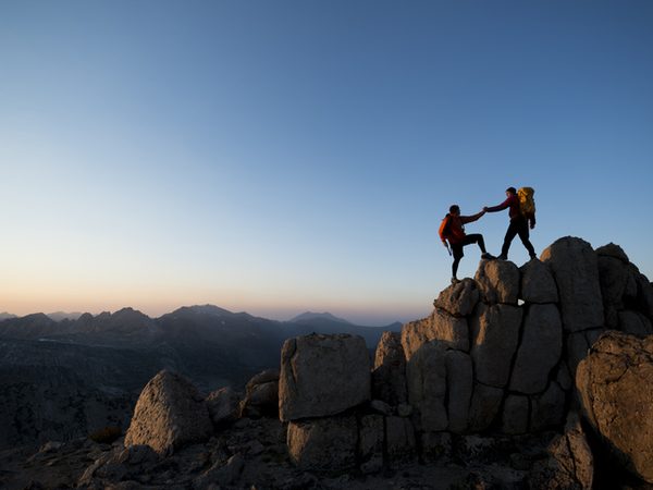 Ein Wanderer gibt einem anderen die Hand in den Bergen