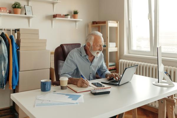 Älterer Mann sitzt am Schreibtisch am Laptop