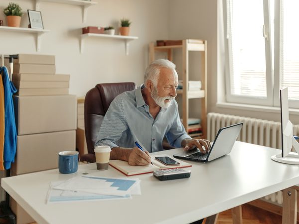 Älterer Mann sitzt am Schreibtisch am Laptop