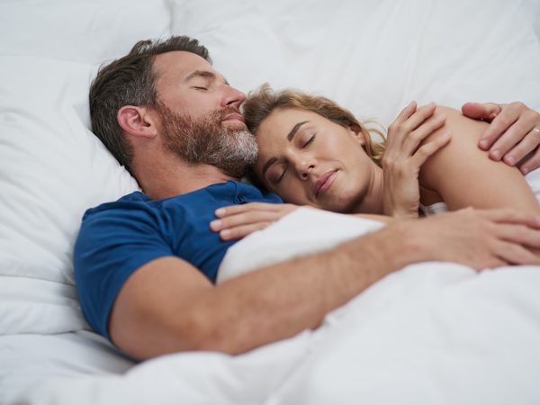 Paar schläft Arm in Arm im Bett.