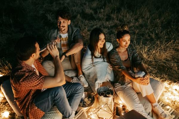 Zwei Männer und zwei Frauen sitzen abends auf einer Wiese am Lagerfeuer
