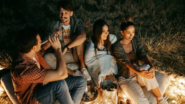 Zwei Männer und zwei Frauen sitzen abends auf einer Wiese am Lagerfeuer und schützen sich vor Mücken.