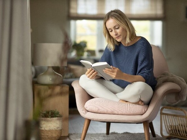 Frau hat es sich in einem Sessel bequem gemacht und liest in einem Buch über Schlafstörungen.
