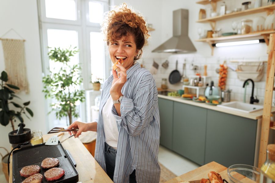 Frau steht in der Küche und kocht. Sie probiert ein Stück Baguette