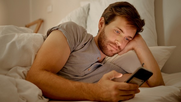 Mann liegt im Bett und schaut auf sein Smartphone