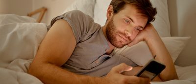 Mann liegt im Bett und benutzt sein Handy