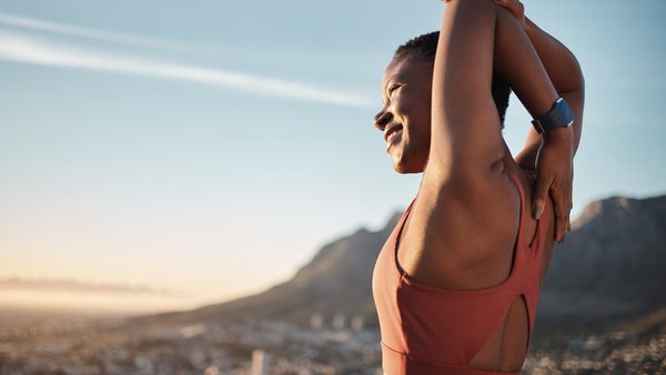 Frau dehnt sich in der Natur – Regelmäßige Bewegung zur Linderung von PMS-Symptomen.