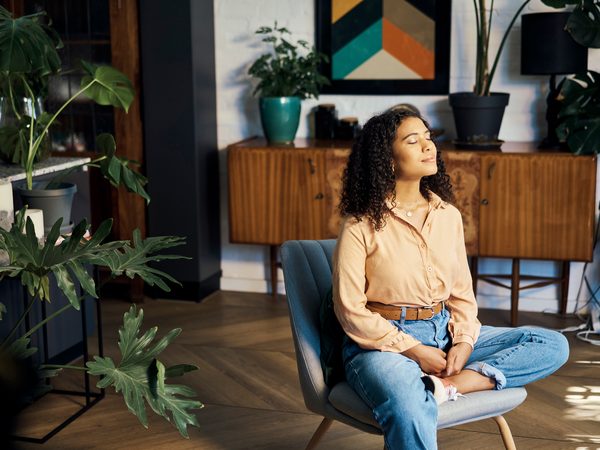 Frau sitzt im Schneidersitz auf einem Stuhl im Wohnzimmer