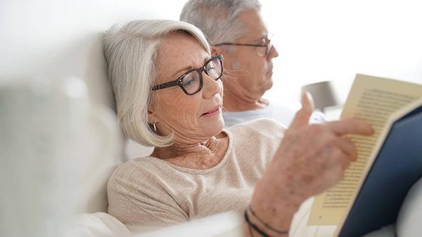 Ehepaar liegt entspannt im Bett. Die ältere Frau liest noch ein Buch.