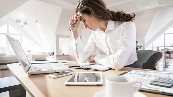 Frau stützt sich am Schreibtisch erschöpft den Kopf
