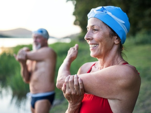 Älteres Paar wärmt sich vorm Schwimmen im See auf.