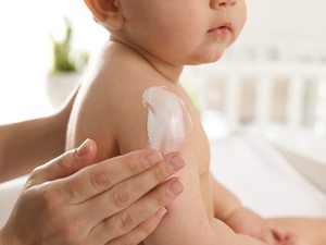 Baby wird auf der Schulter eingecremt